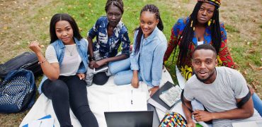 group-five-african-college-students-spending-time-together-campus-university-yard-black-afro-friends-sitting-grass-studying-with-laptops